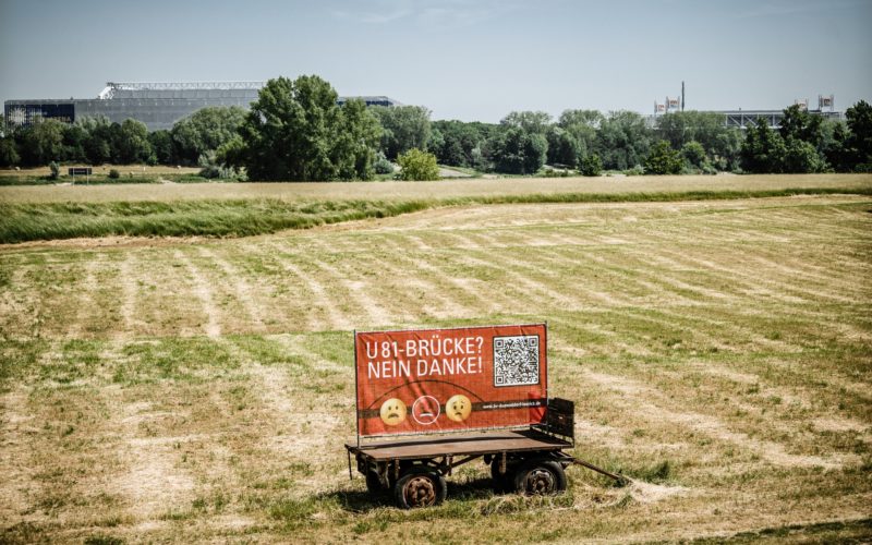 Etwa an der Stelle, auf dem Bürger*innen gegen eine U81-Brücke protestieren, würde das Bauwerk über den Rhein kommen. Im Hintergrund: Arena und Messe. Foto: Andreas Endermann