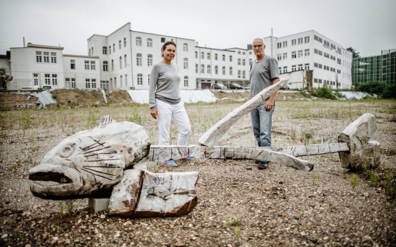 Hilli Hassemer und Peter Ripka vor der großen Fischgräte, die neben der ehemalige Liesegang-Fabrik liegt und um die herum im August Blumenkreise blühen. Foto: Andreas Endermann